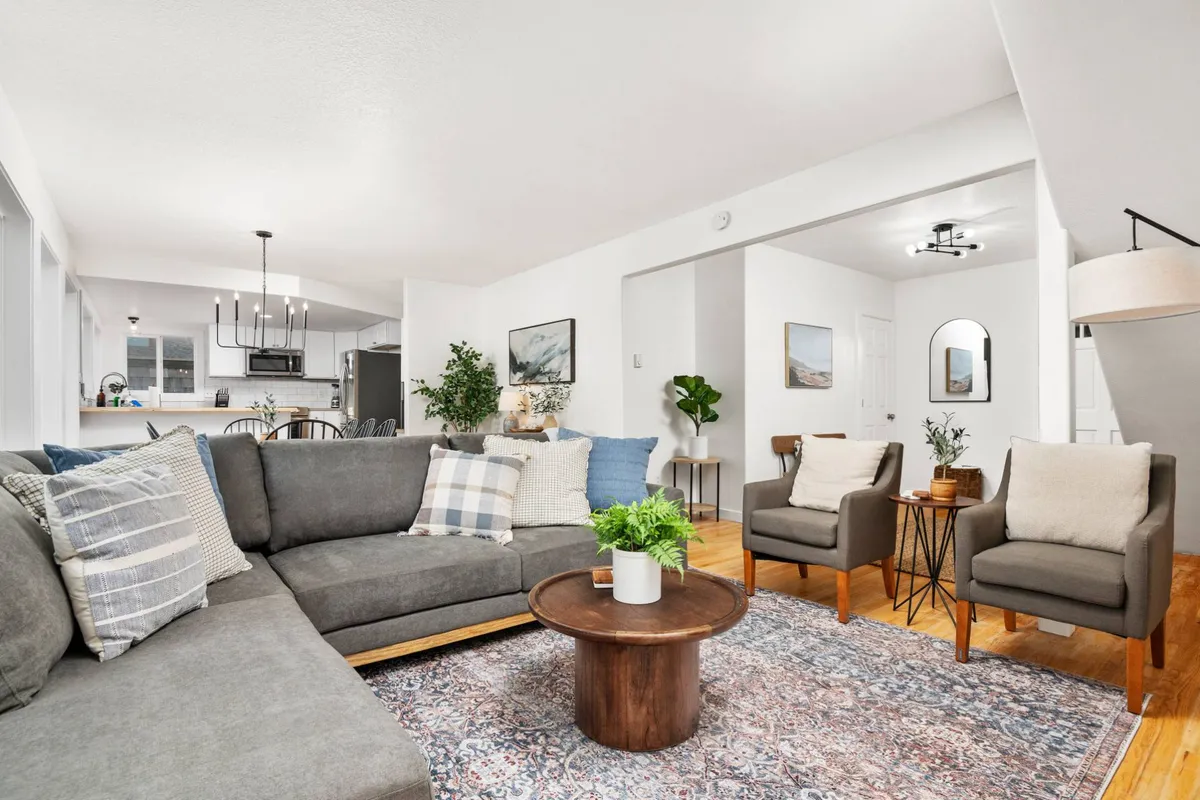 A cozy living room scene with a plush sectional sofa, wooden coffee table, decorative pillows, and artwork adorning the walls. The space feels airy and welcoming, ideal for lounging, reading, or sharing stories with friends and family.