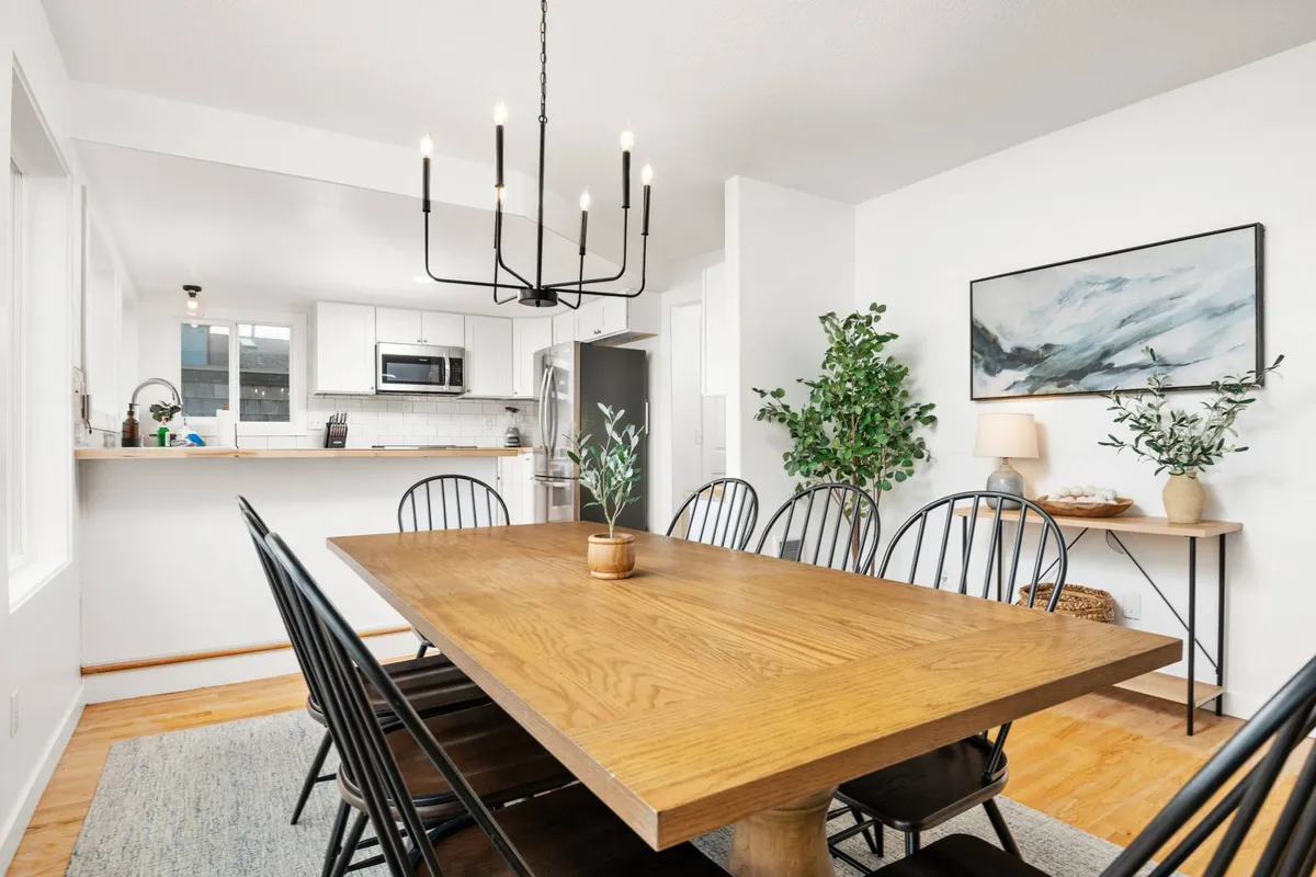 This image showcases a warm, welcoming dining area with a wooden table, chandelier, green plants, and artwork on the wall. The setting is intimate and inviting, ideal for gathering family or friends after a day of exploring local culture and flavors.