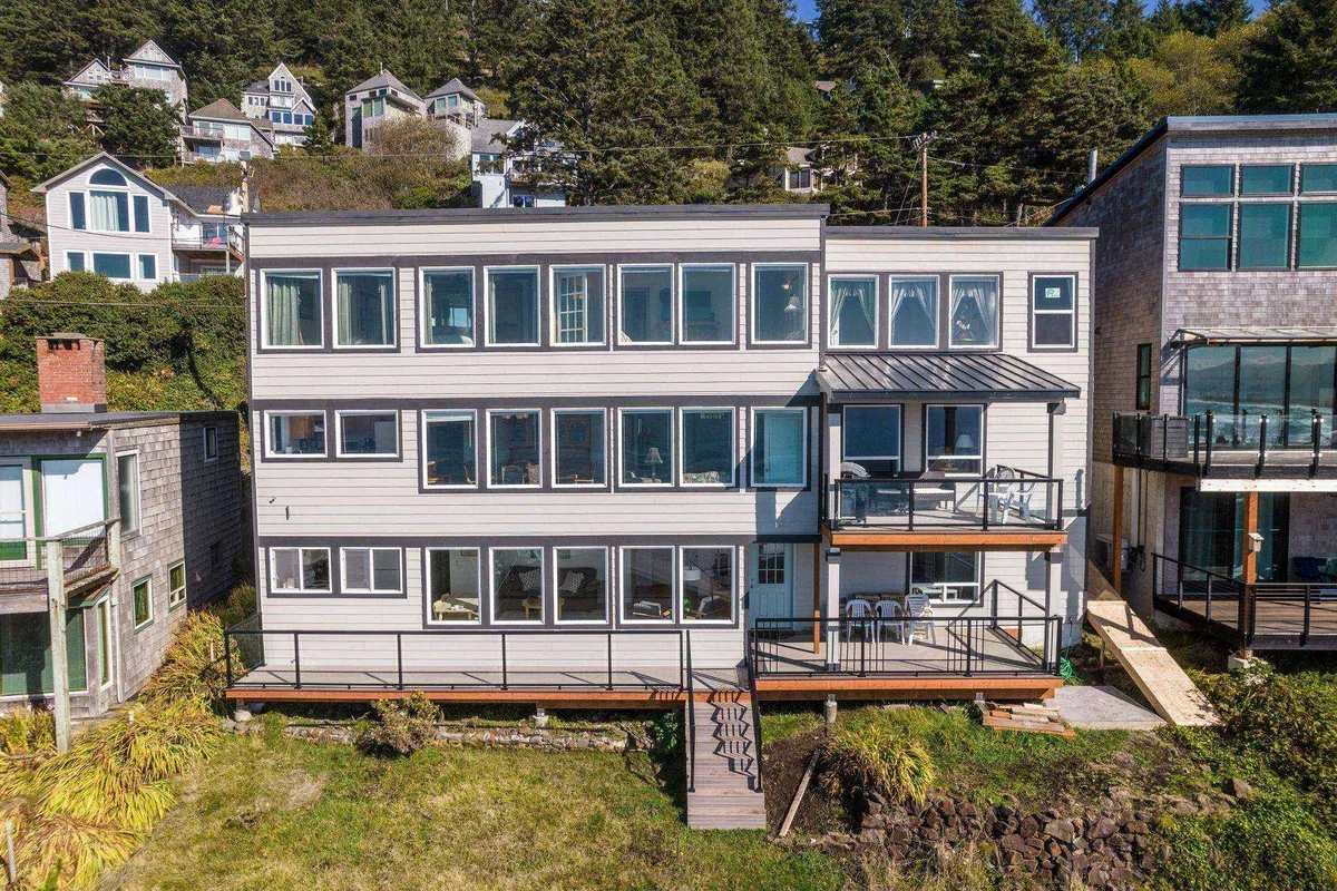 This exterior image showcases the home's large windows, a spacious deck area, and abundant surrounding greenery. The deck offers a welcoming space for guests to relax outdoors, enjoy scenic views, or watch their dogs play in a safe environment.