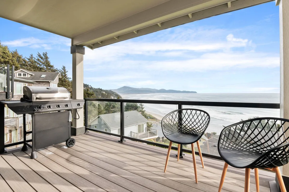A scenic exterior setting with a grill ready for barbecuing, comfortable chairs, and a sweeping view of the ocean. The relaxed mood invites guests to enjoy sunset dinners outdoors while taking in the coastal breeze.