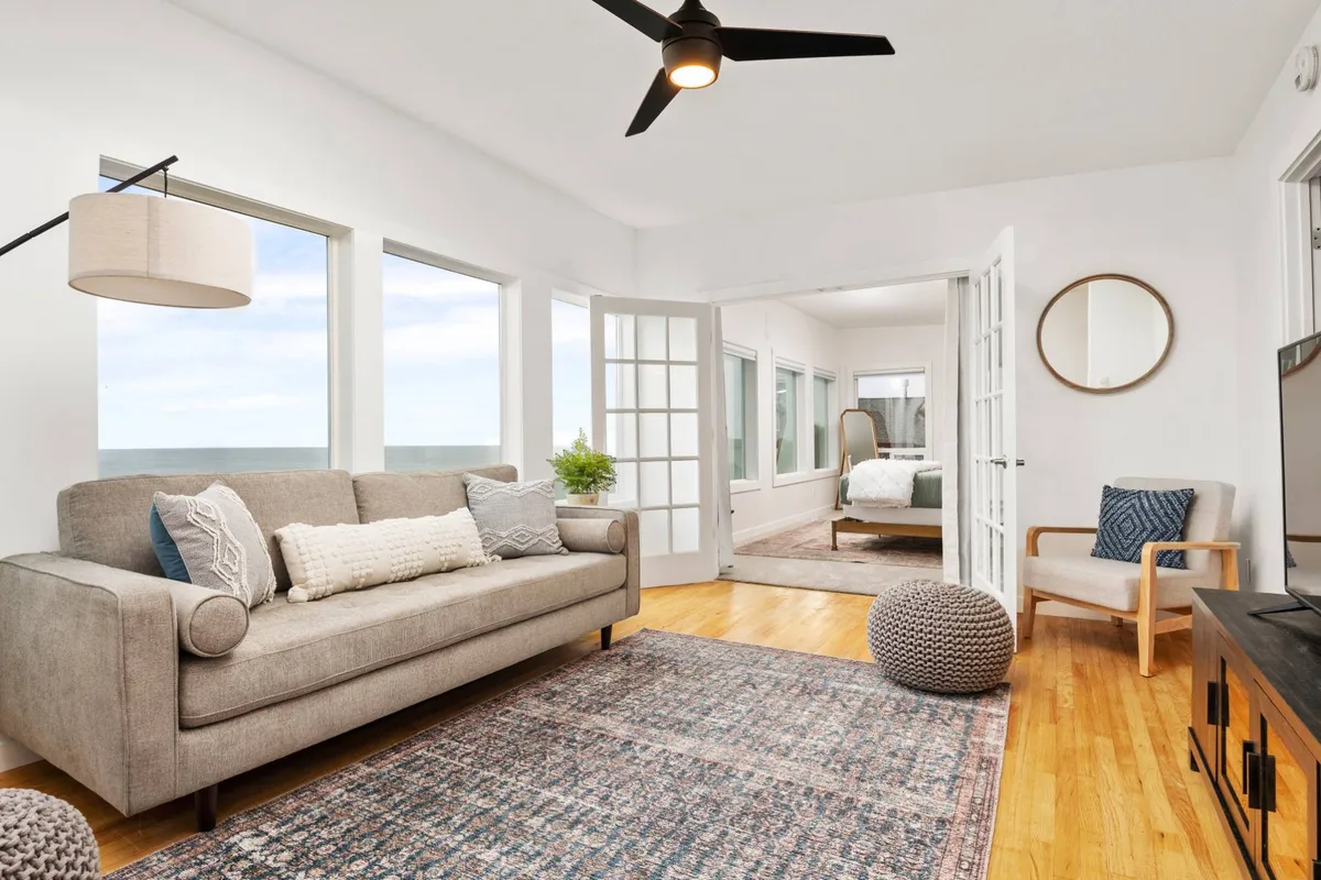 A bright upstairs lounge area with a comfortable sofa, large windows providing ample natural light, a decorative rug, and an armchair. The space feels airy and relaxing, perfect for reading, socializing, or quiet downtime after a day outside.