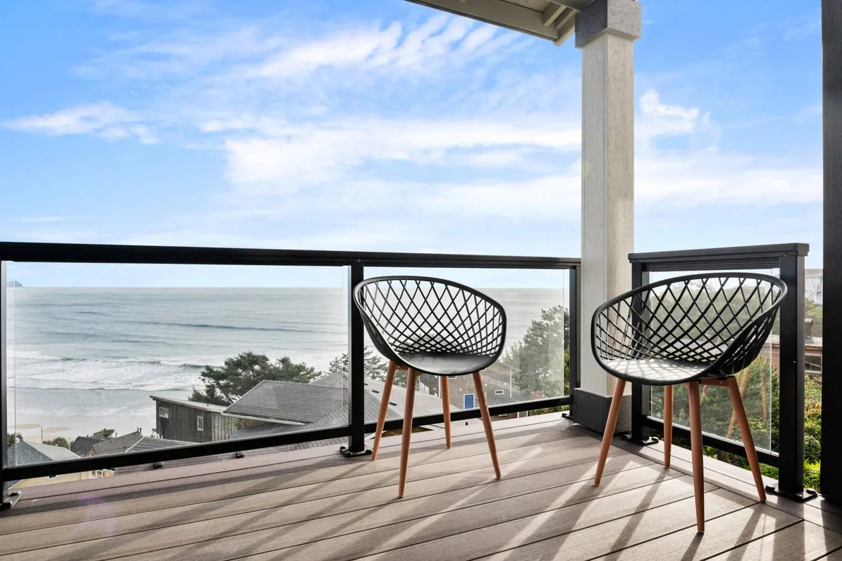 An inviting outdoor seating area with two black woven chairs facing a sweeping ocean view under a clear sky. The spot suggests a perfect setting for enjoying morning coffee or unwinding at sunset while listening to the gentle sounds of the Pacific.