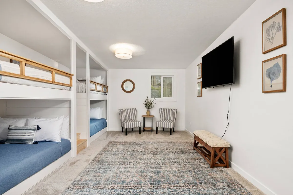 A family-friendly bunk room featuring playful bunk beds, a cozy seating area, decorative wall art, and a television. The room evokes a sense of fun and comfort, ideal for children or young adults to unwind after a busy day exploring.